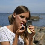 A woman applying primer to her face in preparation for a summer makeup routine in New York City