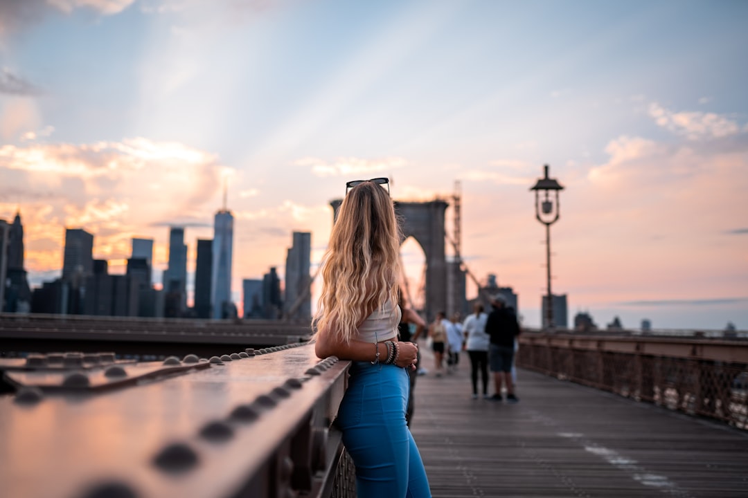 A woman frames the Brooklyn Bridge in warm morning light, a classic outdoor photography spot in NYC