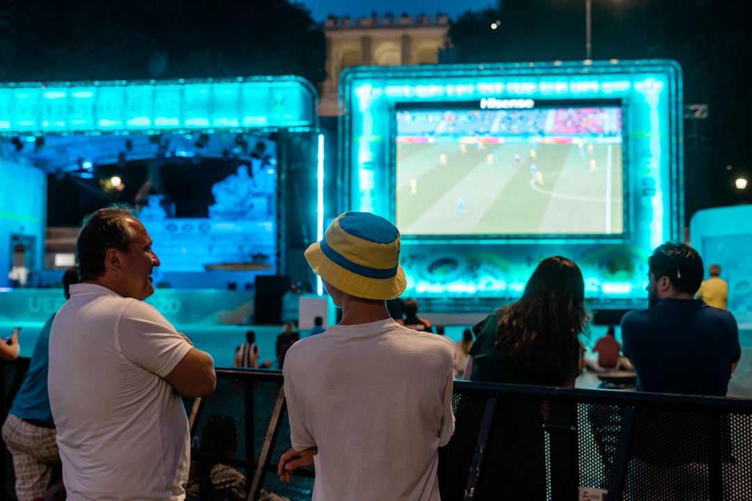A crowd of fans cheering at one of the FIFA World Cup fan zones on a large outdoor screen in New York City