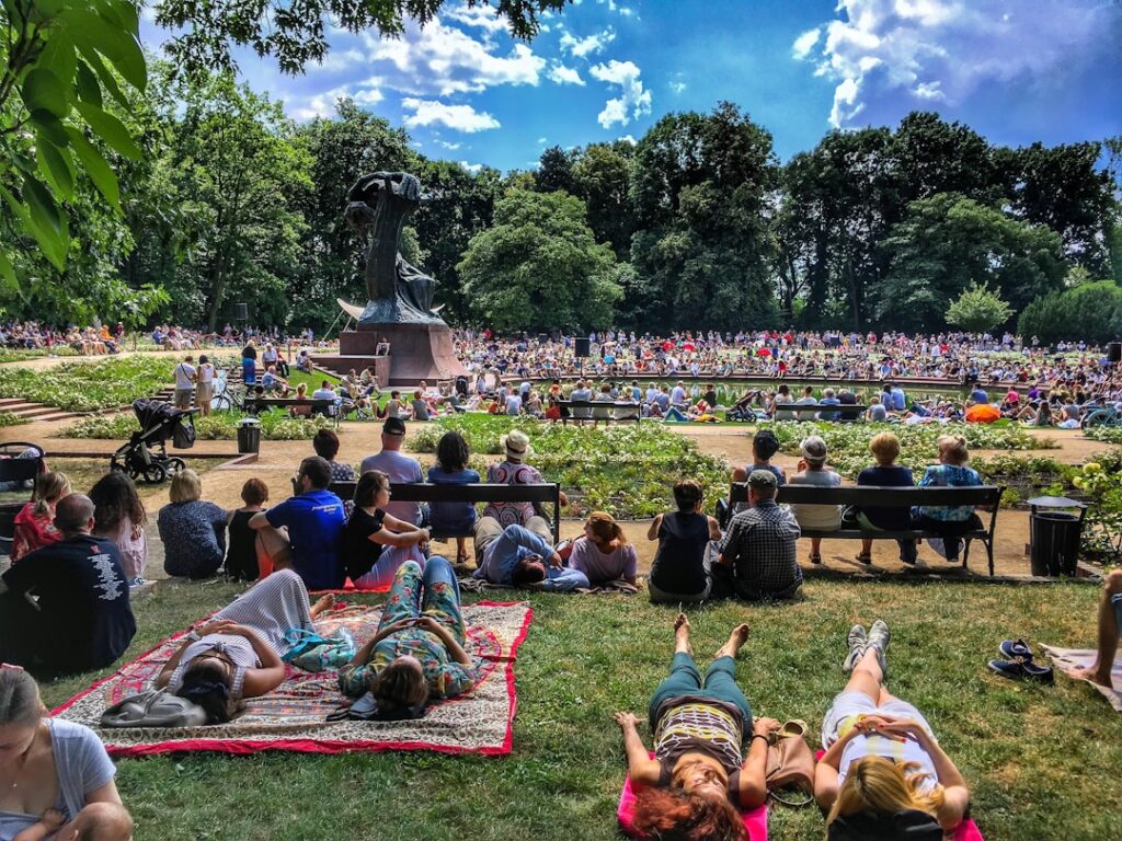 A diverse crowd of people enjoying free outdoor concerts in a New York City park on a summer evening