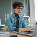 A freelancer pauses at her desk to manage burnout by stepping back from her screen and breathing