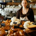 A woman carefully selecting a pastry at a gluten-free bakeries counter in New York City, surrounded by baked goods.